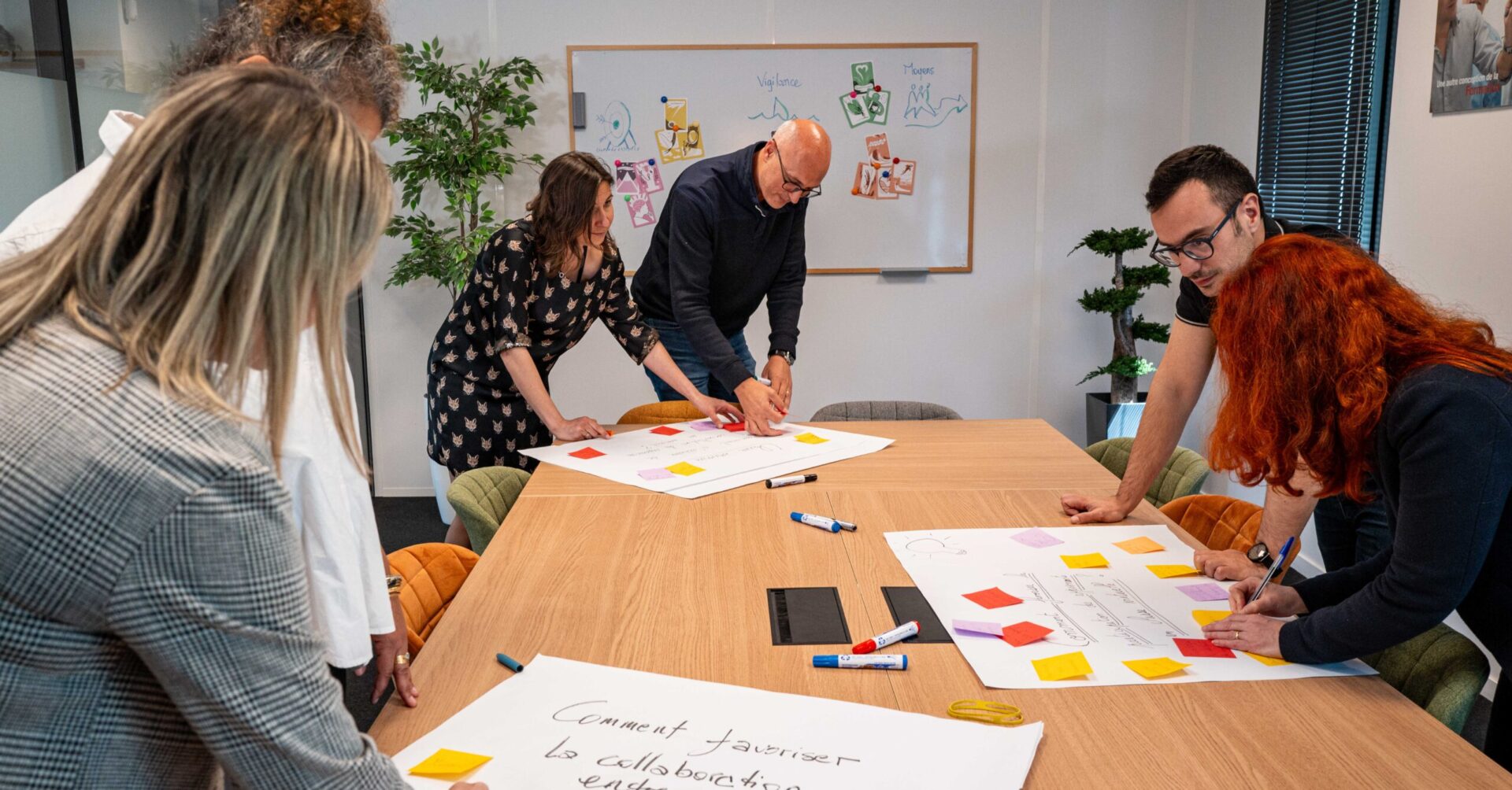 Groupe de personnes collaborant autour d'une table avec des post-its et des schémas.