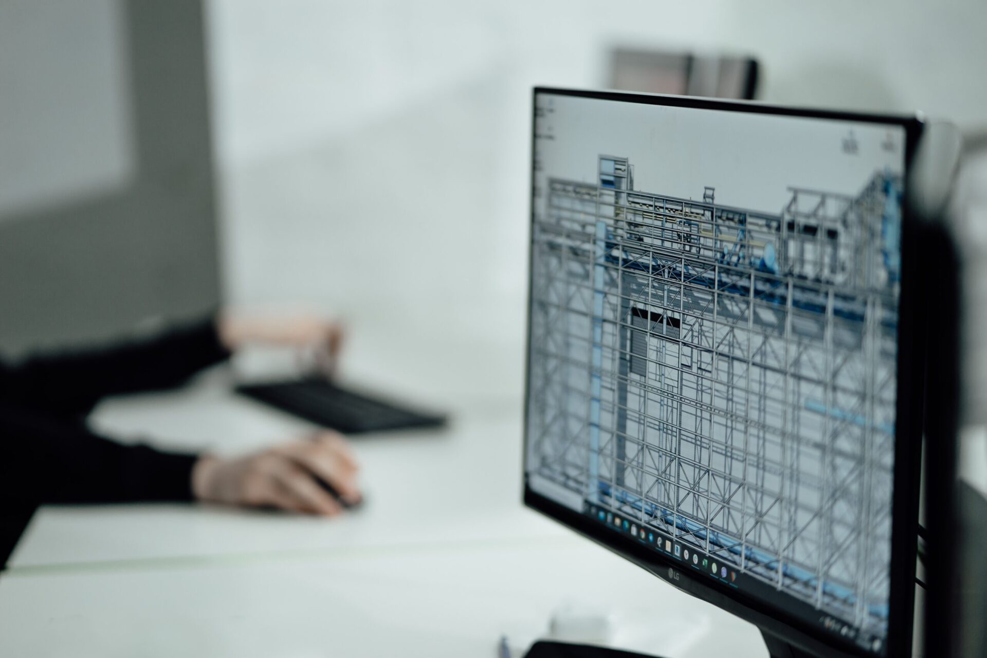 Écran affichant une maquette 3D de structure métallique avec une personne travaillant en arrière-plan.