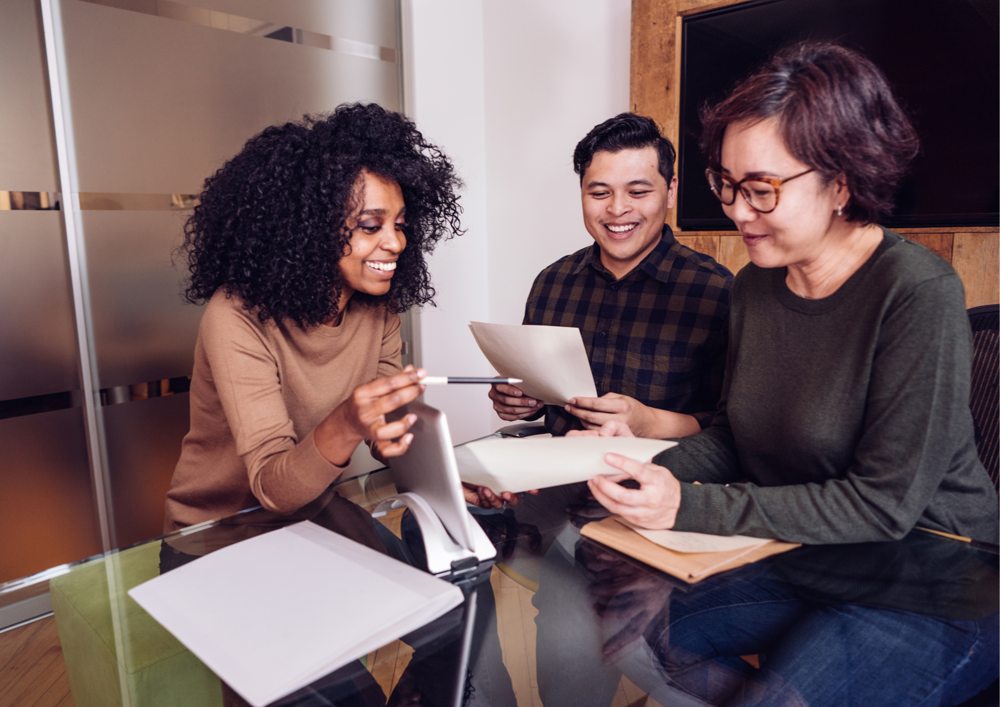 Trois professionnels échangent autour de documents pendant une réunion de travail.