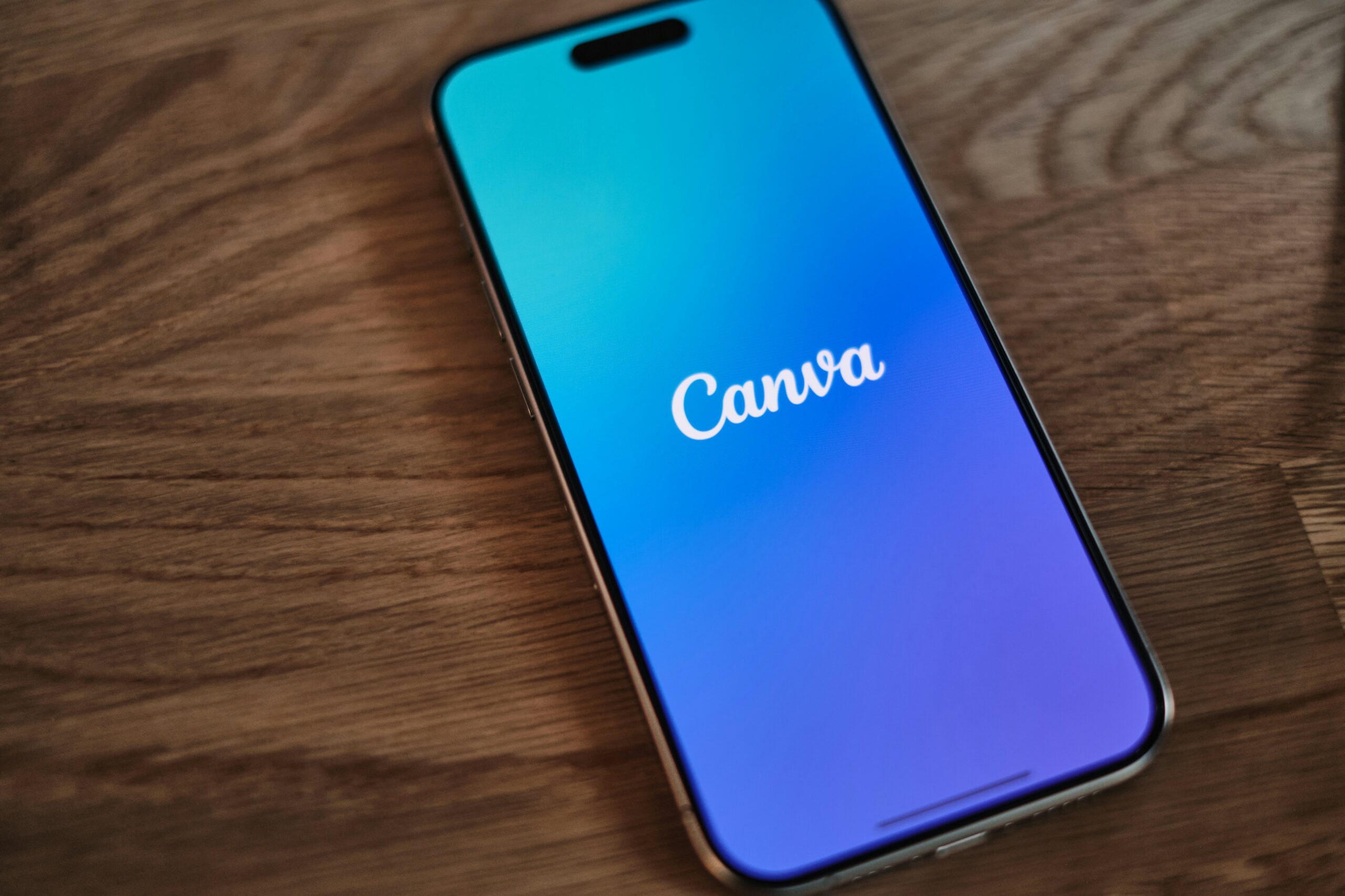 Application Canva affichée sur un smartphone posée sur une table en bois