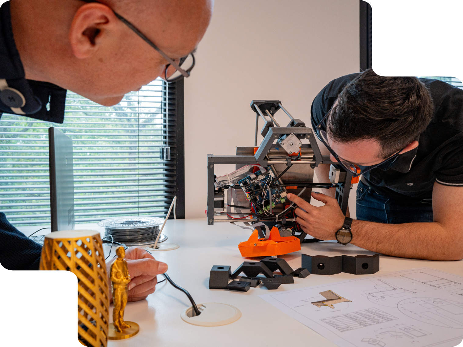 De la conception à la réalisation en 3D Deux hommes travaillant sur une imprimante 3D avec des objets techniques.