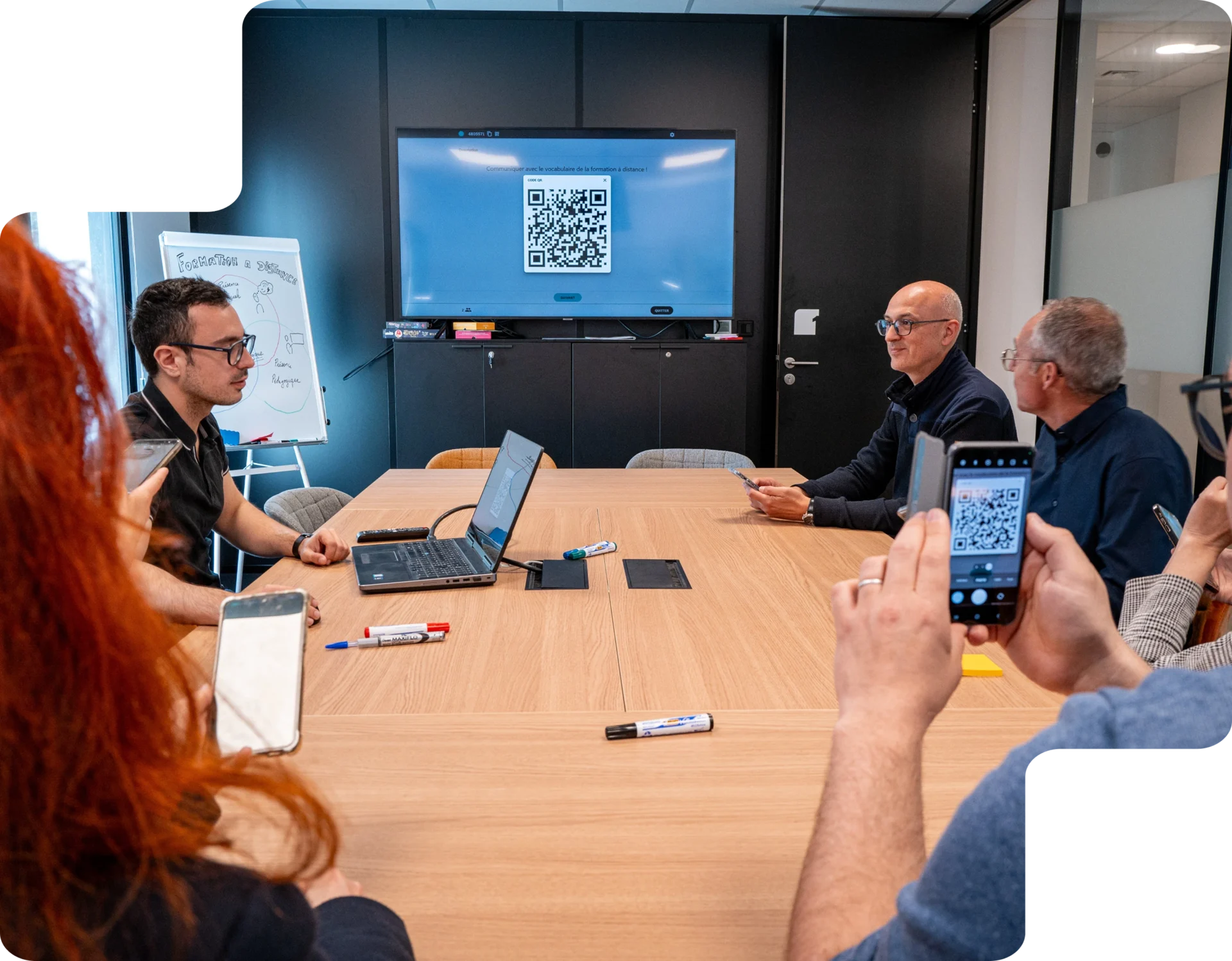 Un groupe de personnes en formation utilise leurs smartphones pour scanner un QR code affiché sur un écran de présentation